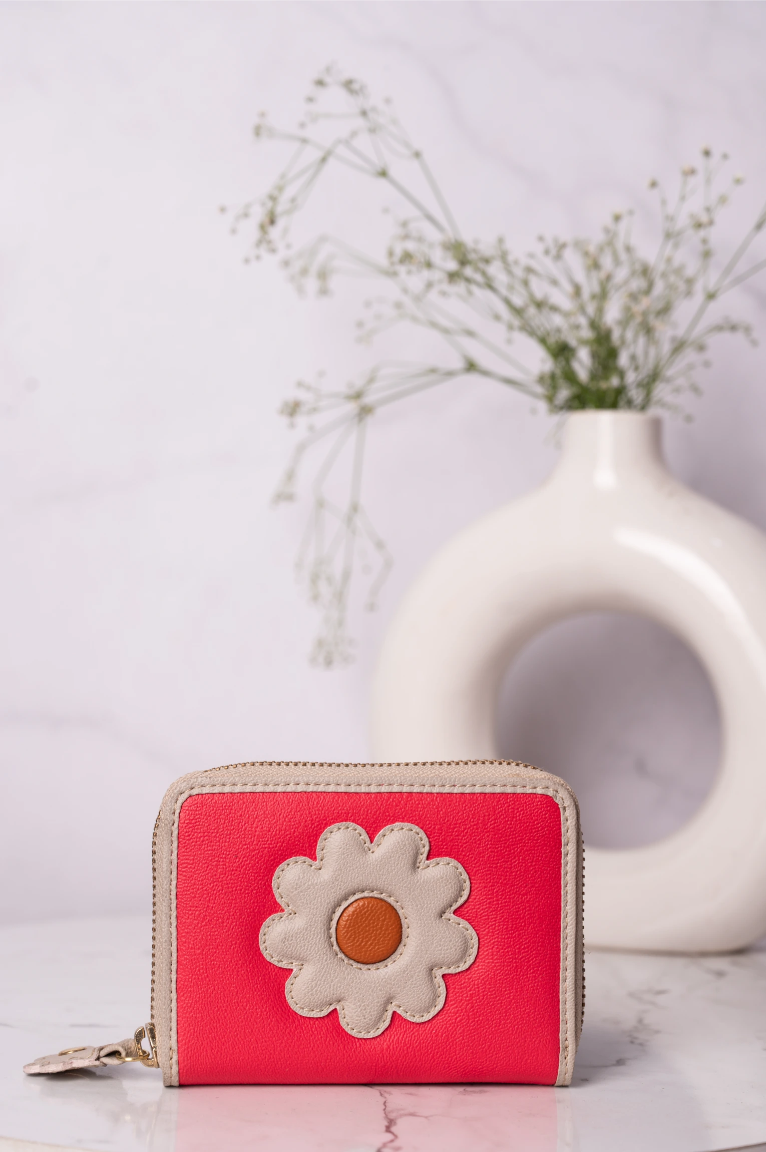 Pink vegan leather wallet for women with a flower design on a light surface with a vase in the background
