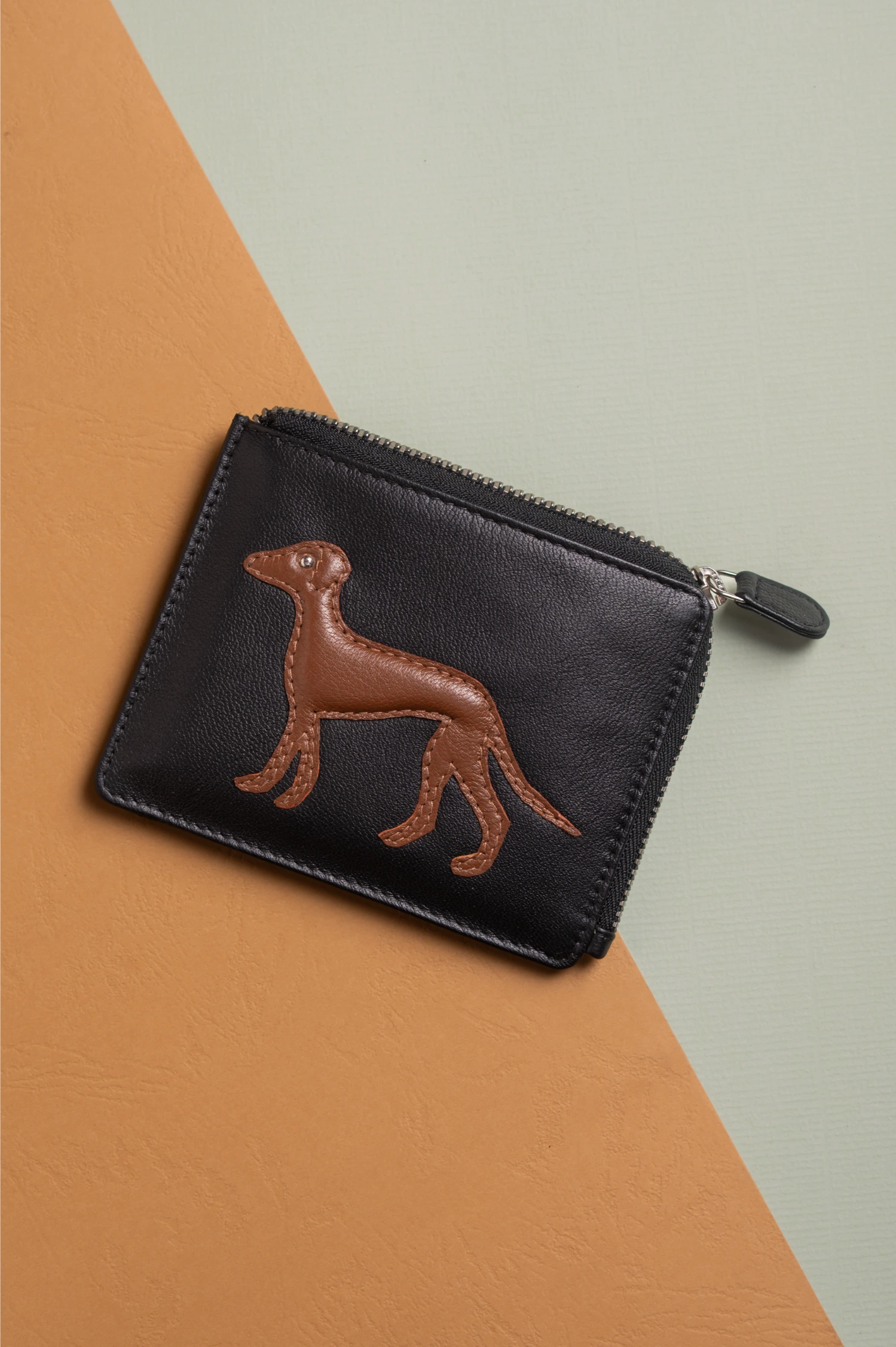 Black vegan leather pouch for women with brown dog illustration on a two-tone background