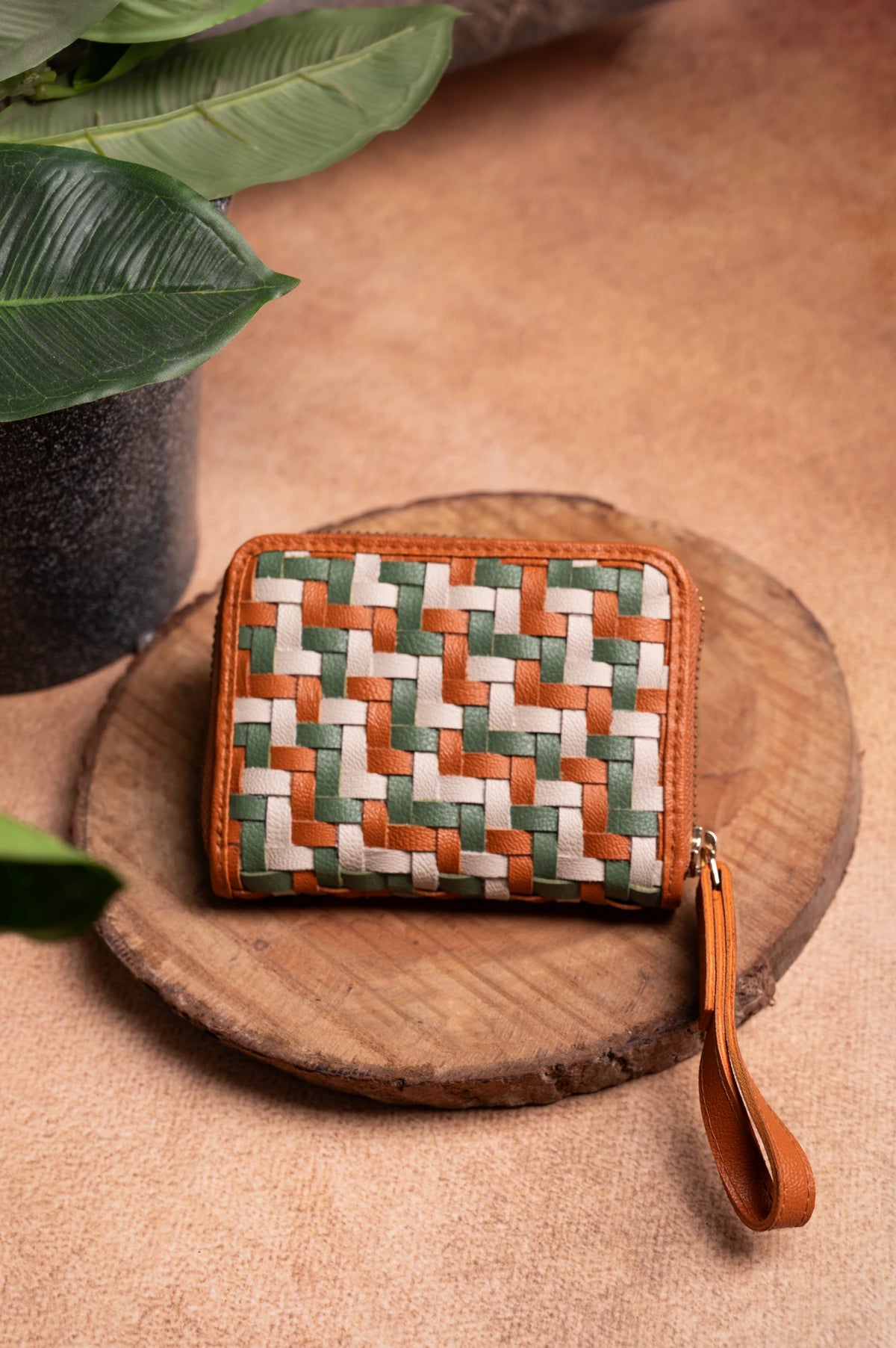 Woven vegan leather wallet for women with a strap on a wooden surface with leaves in the background