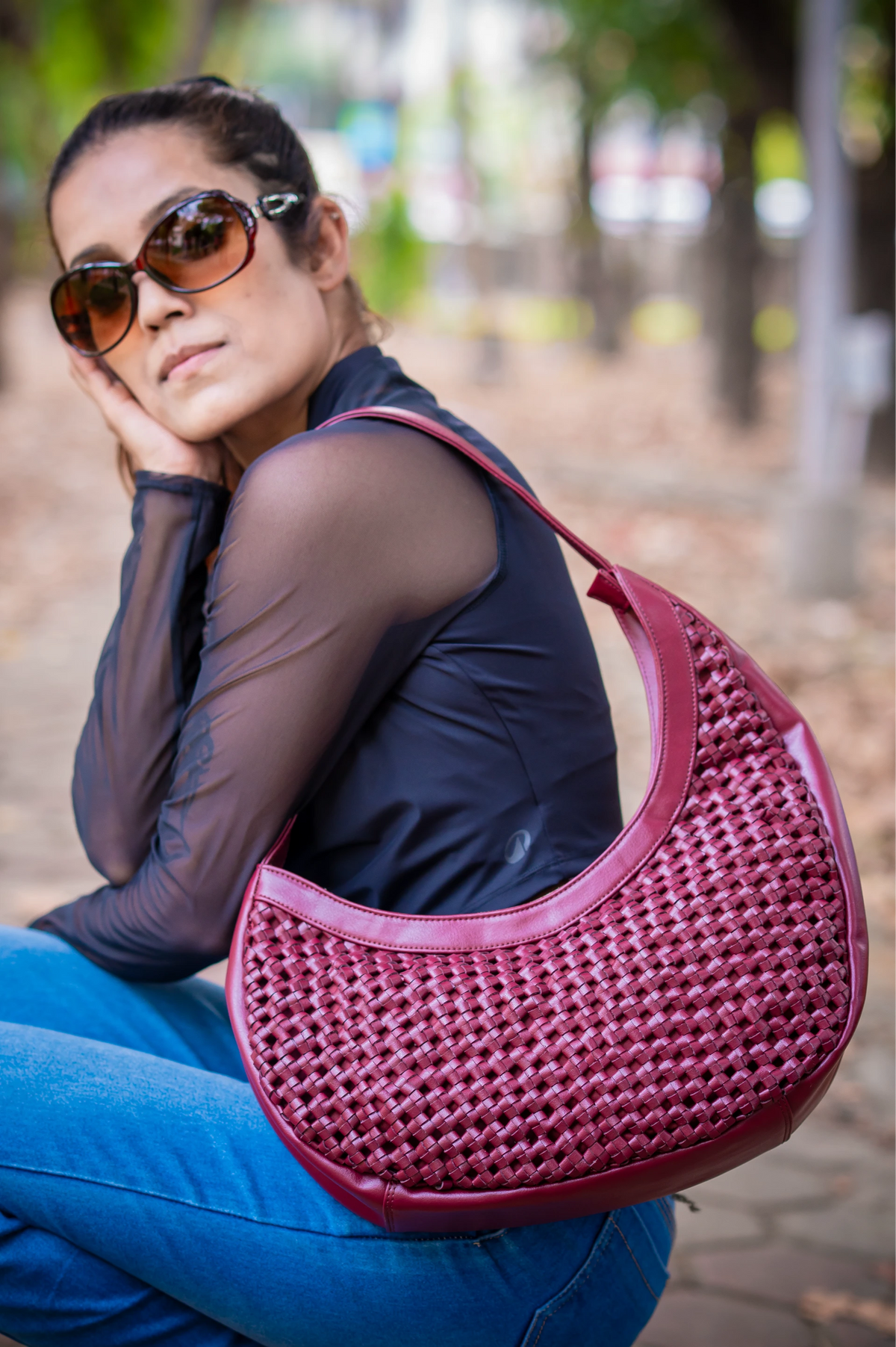 Woman sitting outdoors wearing sunglasses and holding a pink woven vegan leather handbag for women.
