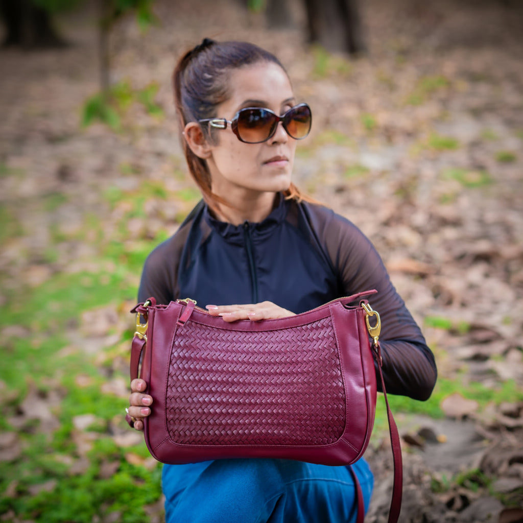 Woman holding a maroon vegan leather handbag for women outdoors with a blurred natural background