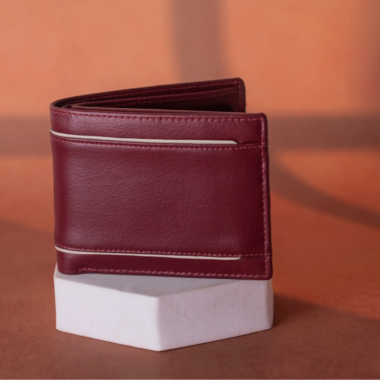 Maroon vegan leather wallet for men on a white stand against an orange background