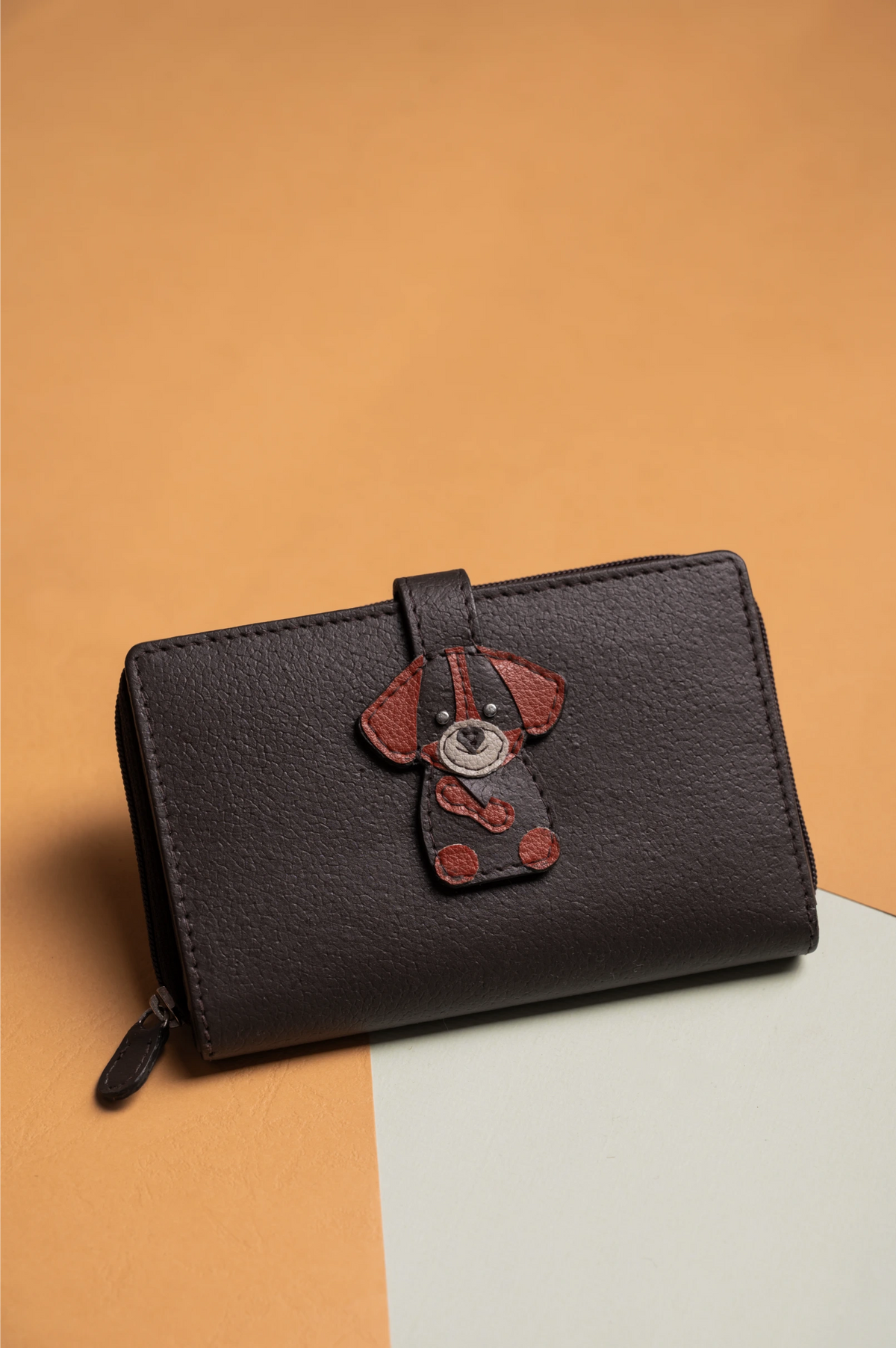 Black vegan leather wallet for women with a dog-shaped patch on an orange and beige background