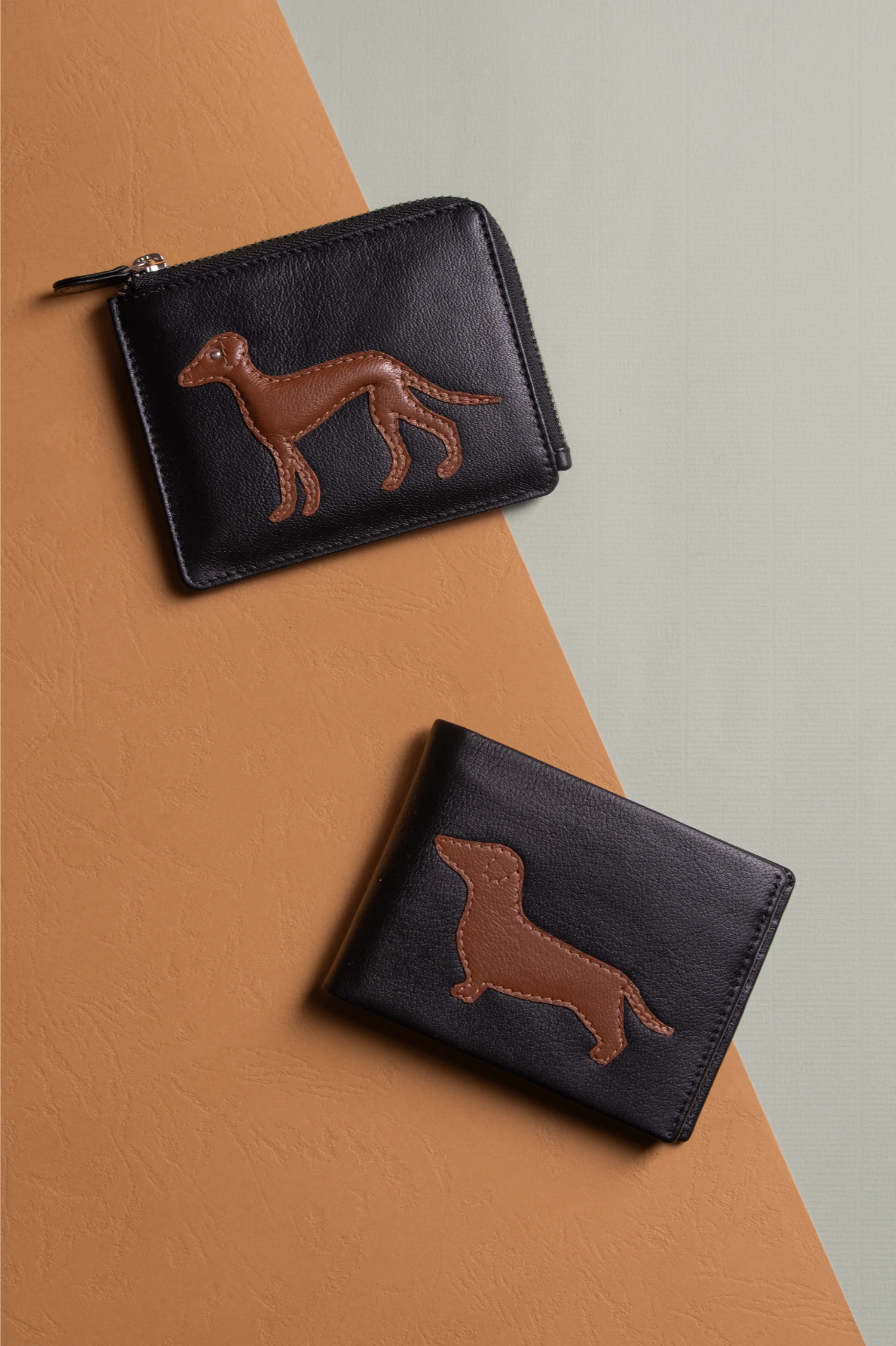 Two black vegan leather wallets for women with brown dachshund illustrations on a brown and gray background