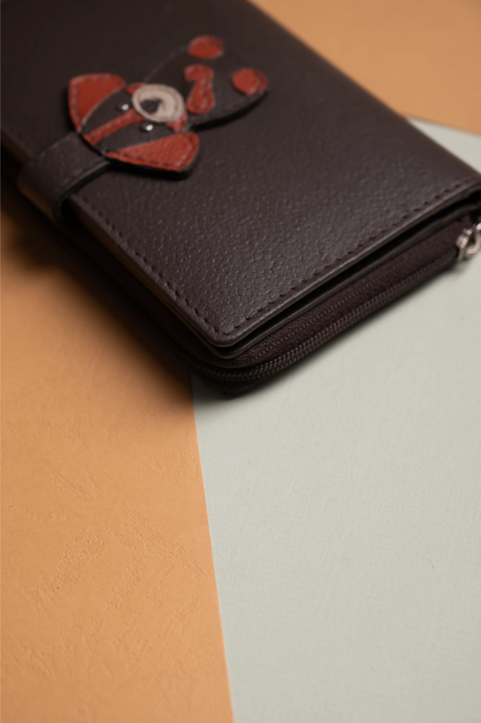 Brown vegan leather wallet for women with a decorative flower charm on a two-tone background