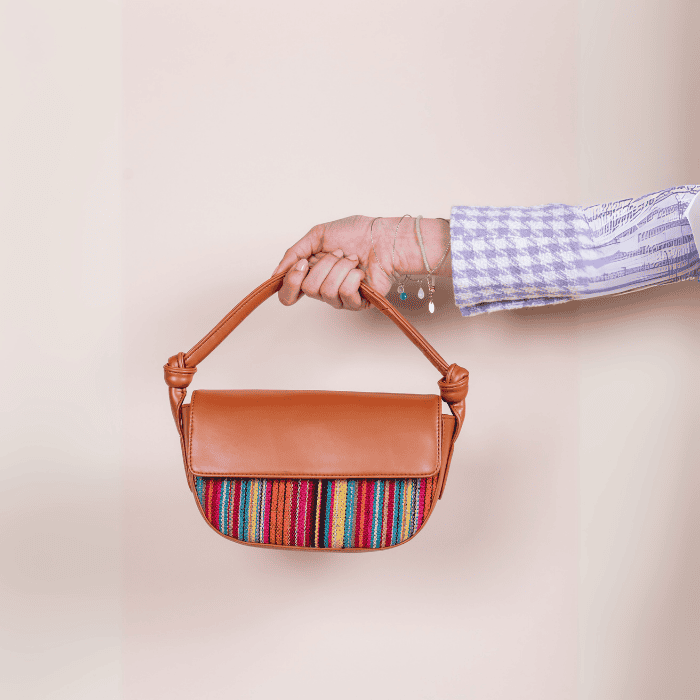 Person holding a brown vegan leather handbag for women with colorful striped pattern on a beige background
