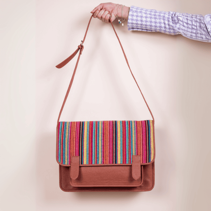 Multicolored striped vegan leather bag for women held by a person against a plain background