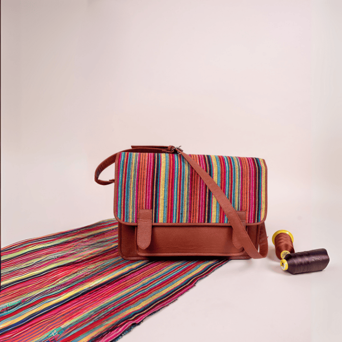 Colorful striped fabric with a brown vegan leather bag for women and spool on a light background
