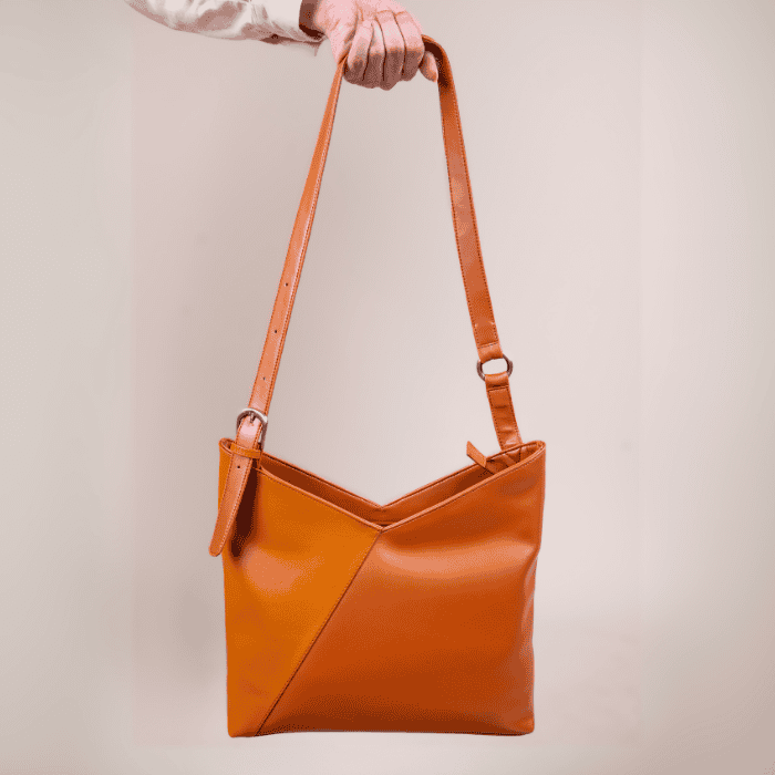 Brown leather vegan leather handbag for women held by a person against a plain background