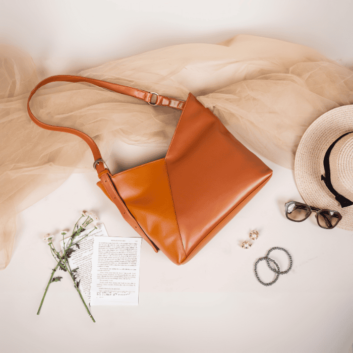 Brown vegan leather handbag for women with a hat, sunglasses, and flowers on a light background