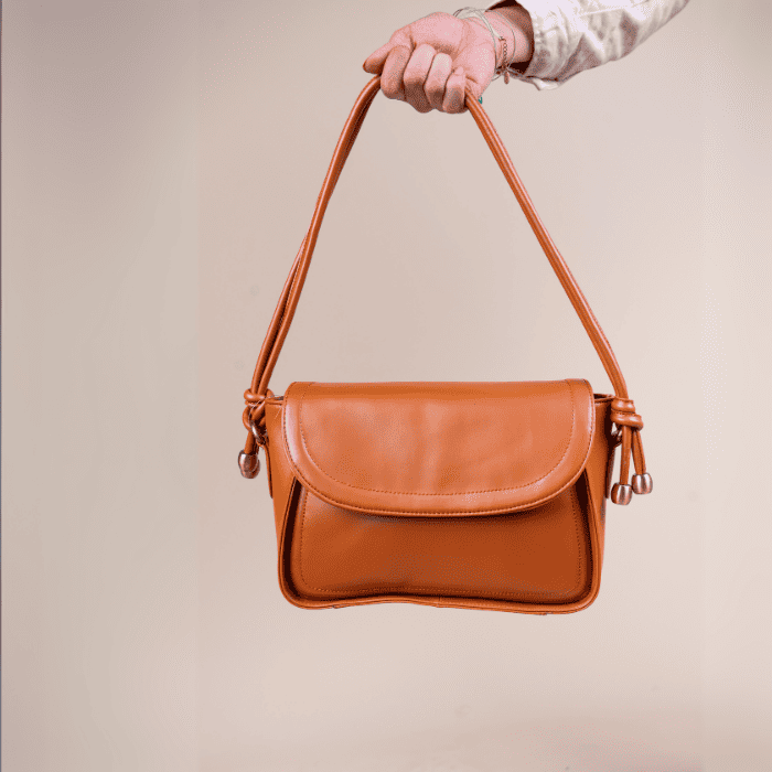 Brown leather vegan leather handbag for women held by a person against a beige background