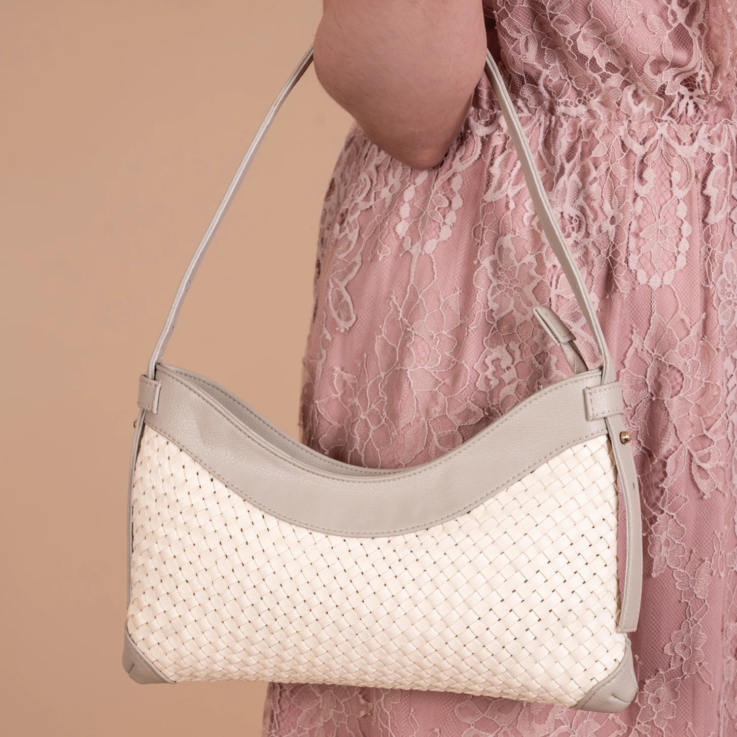 White vegan leather handbag for women with gray strap held by a person wearing a pink lace dress on a beige background
