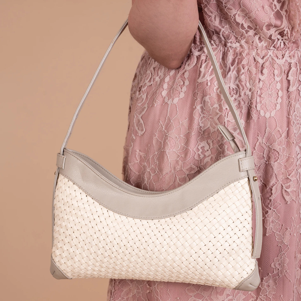 White vegan leather handbag for women with gray strap held by a person wearing a pink lace dress on a beige background
