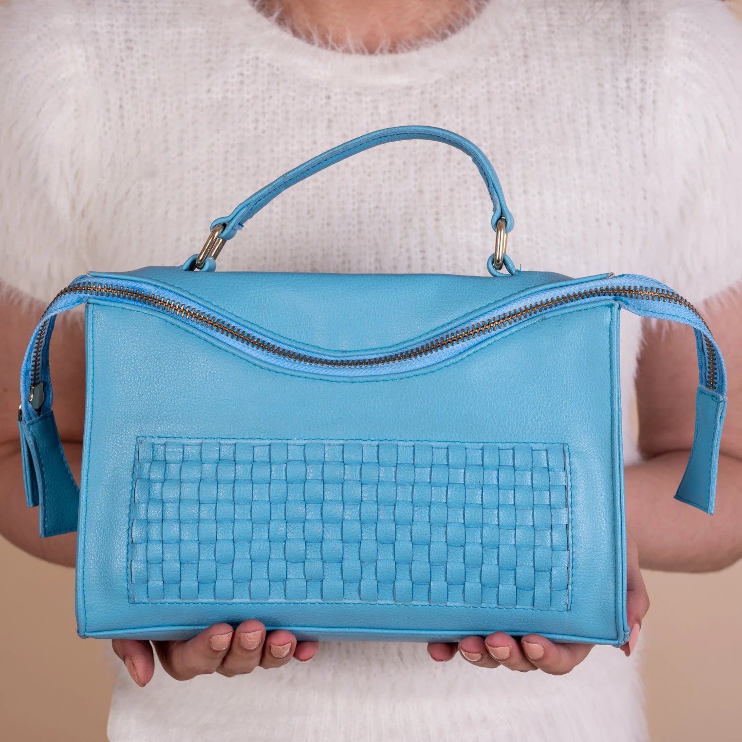 Blue vegan leather handbag for women held by a person wearing a white sweater
