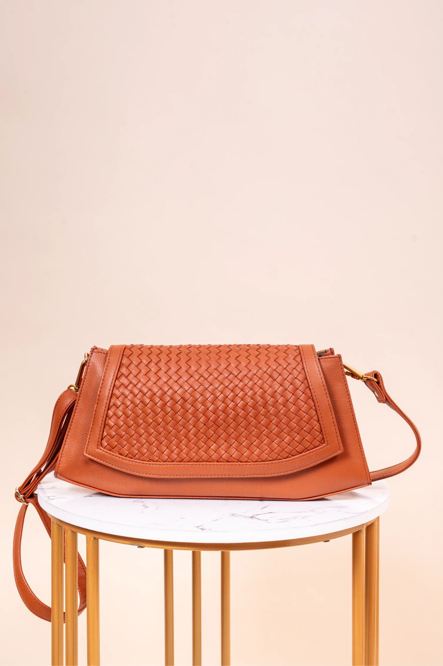 Brown woven vegan leather handbag for women on a white marble surface with a beige background