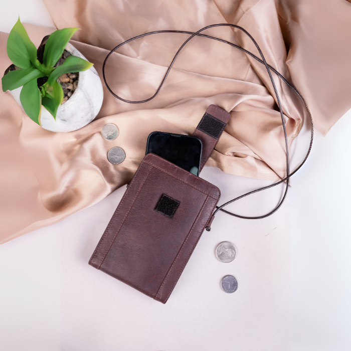 Brown vegan leather wallet with phone pocket on a light pink fabric background with coins and a plant.