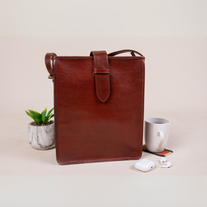Brown vegan leather bag on a light surface with a plant and mug in the background