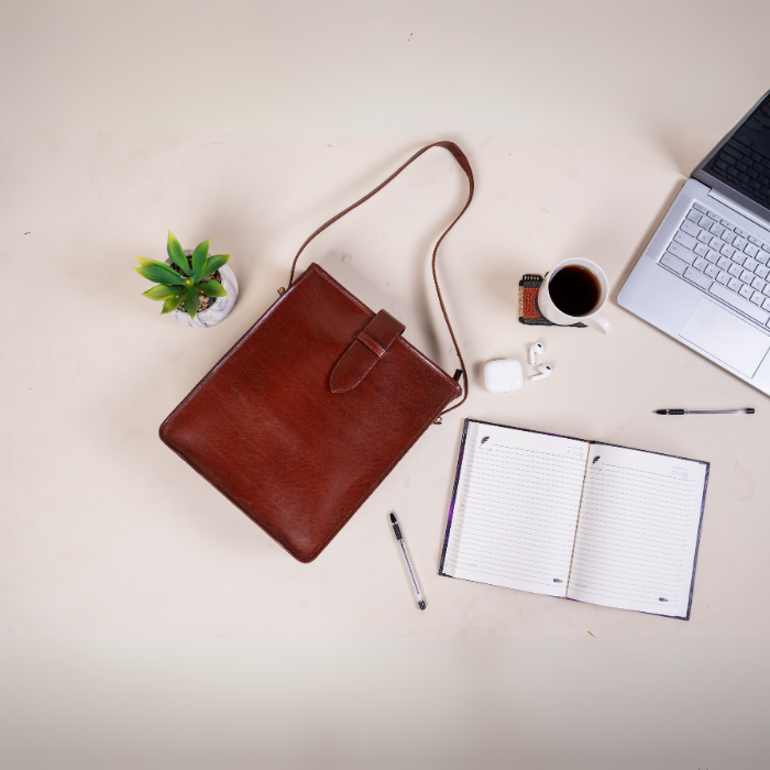 Brown vegan leather bag on a light surface with a laptop, notebook, coffee cup, and plant.
